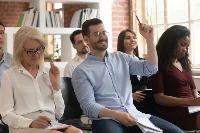 Smiling man raises hand in engaged, diverse adult classroom.